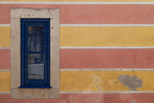 uma janela azul em uma parede amarela e rosa