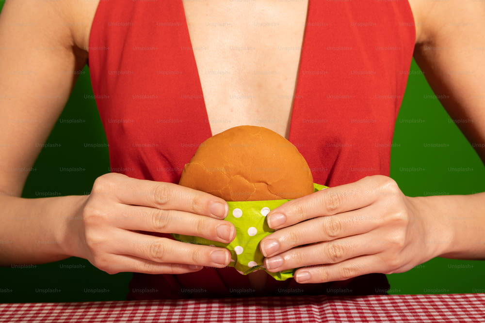 Une femme en haut rouge tenant un sandwich dans ses mains