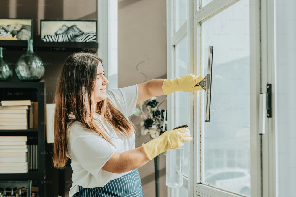 a woman in a white shirt and yellow gloves cleaning a window