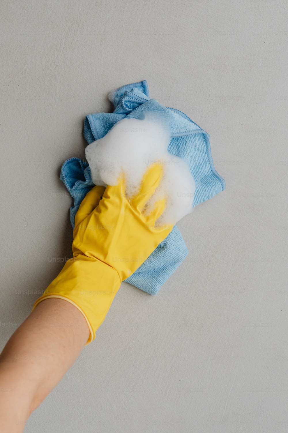 la mano di una persona che indossa guanti di gomma gialli e un panno per la pulizia