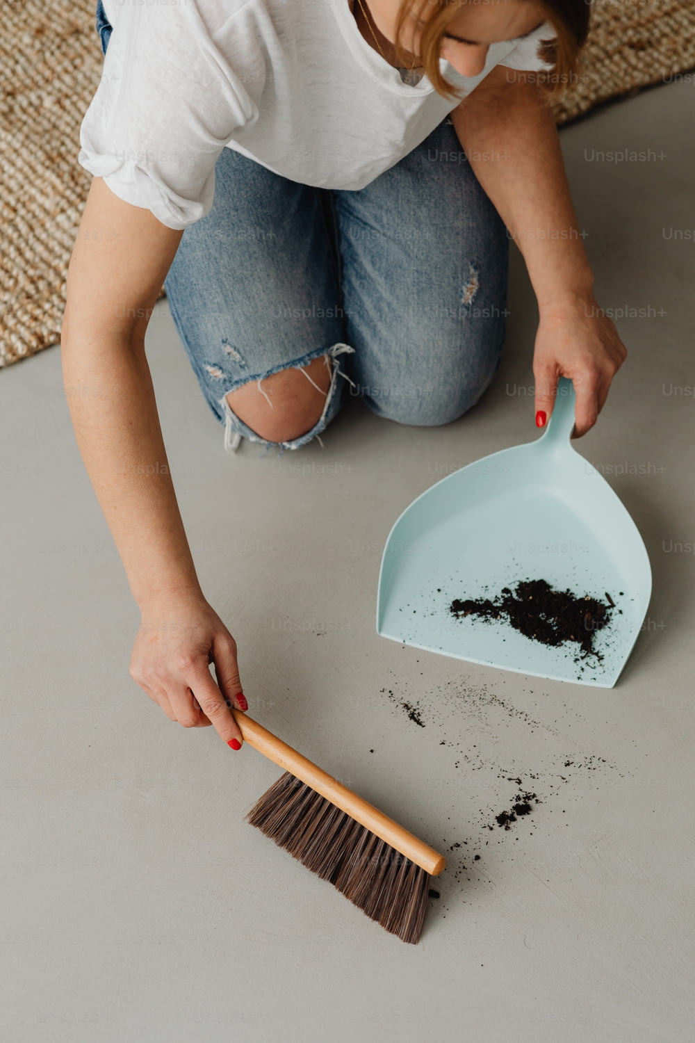 a woman kneeling on the floor with a broom and scoop of dirt