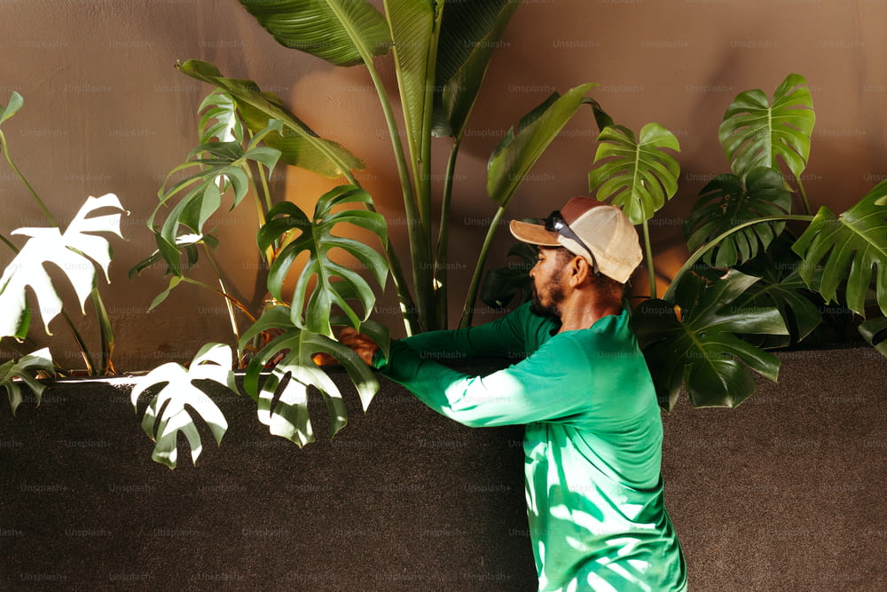 a man in a green shirt and a hat standing next to a plant