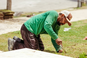 a man in a green shirt and hat digging in the grass