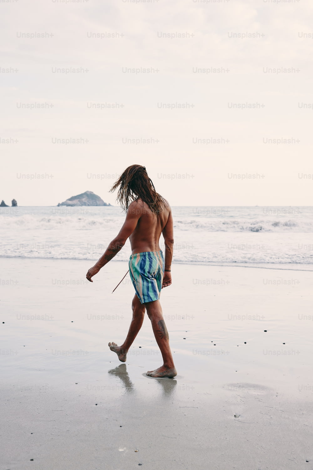 a man with dreadlocks walking on the beach