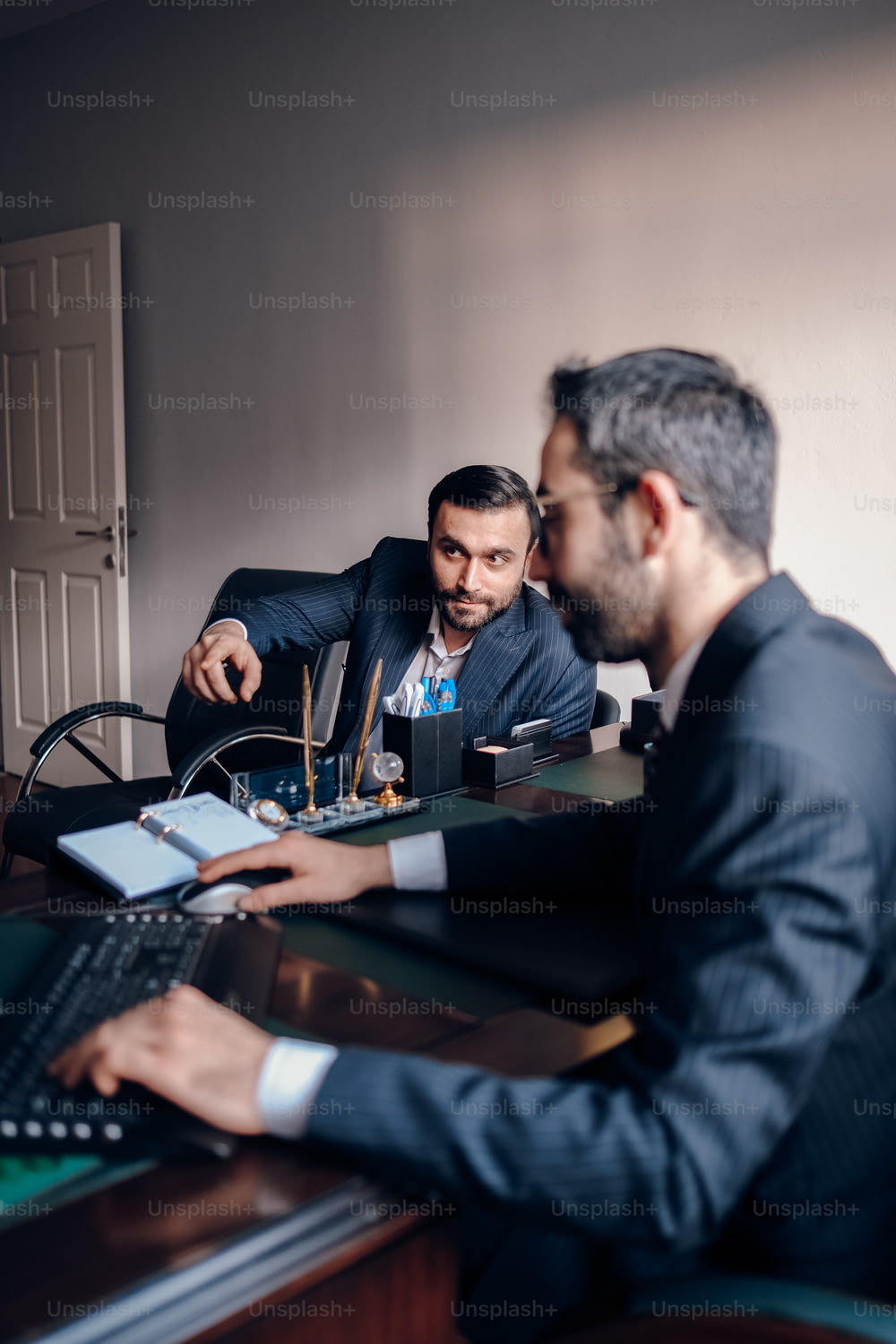 two men sitting at a desk with a laptop