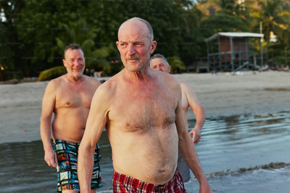 Ein Mann ohne Hemd am Strand neben einem anderen Mann
