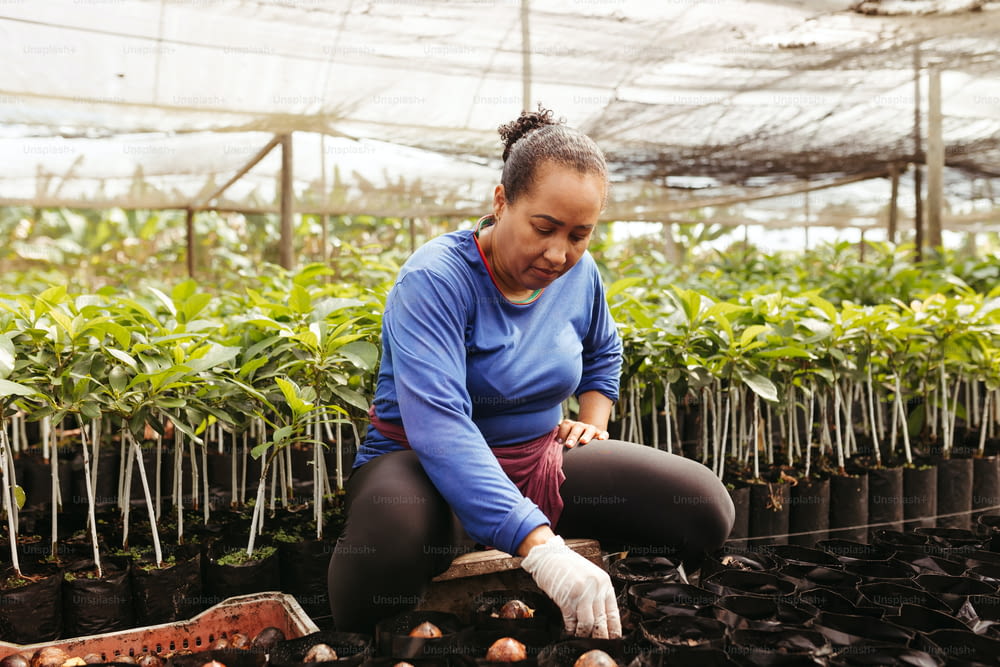 a woman kneeling down in a greenhouse tending to plants