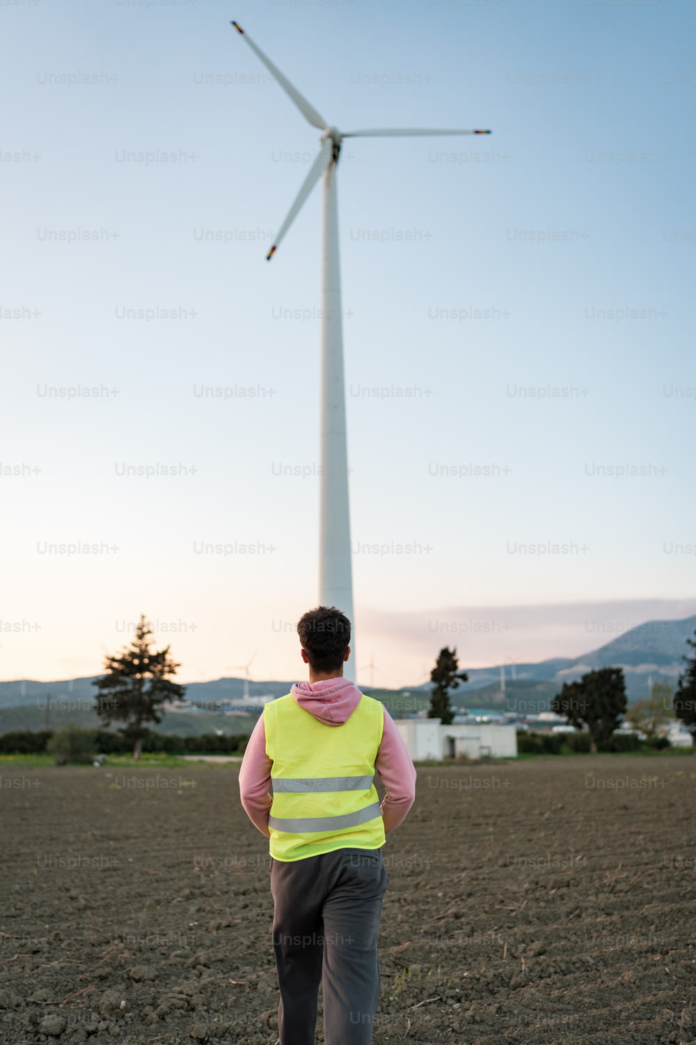 Un hombre con un chaleco amarillo parado frente a una turbina eólica