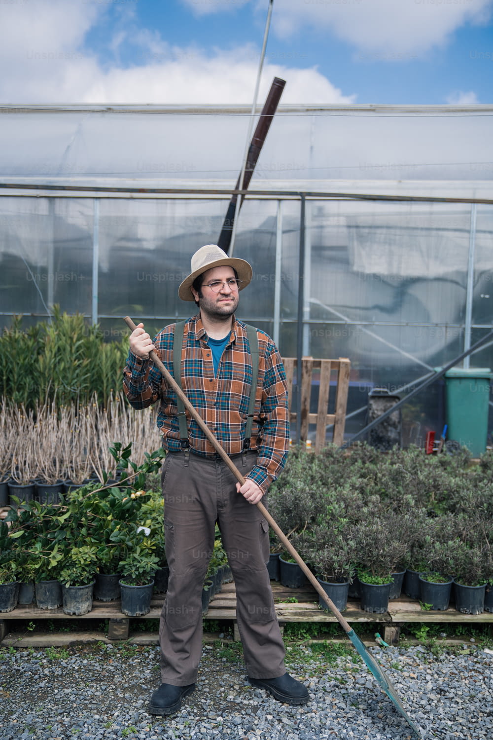 a man in a hat holding a stick in a greenhouse