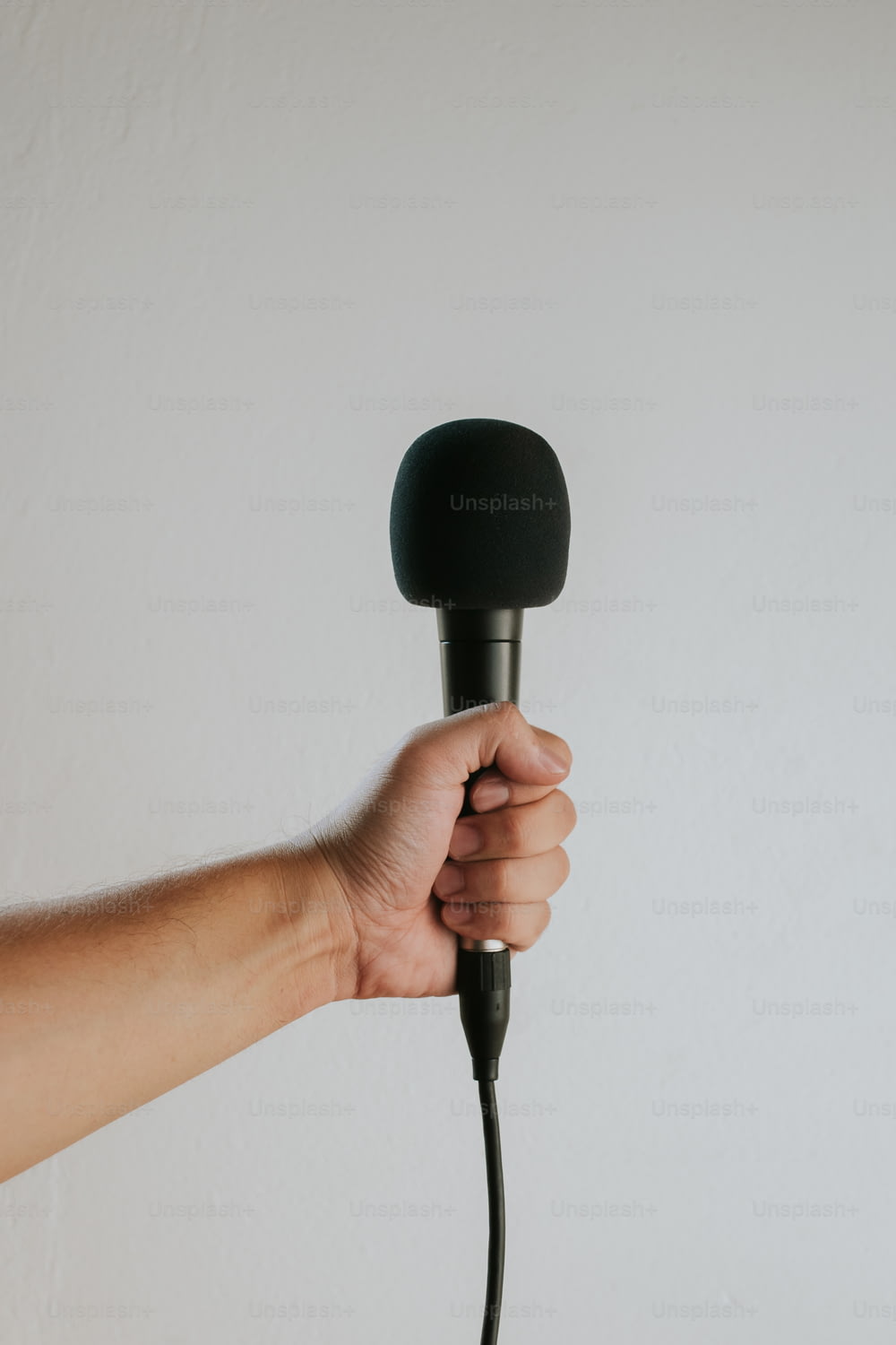 a hand holding a microphone over a white wall