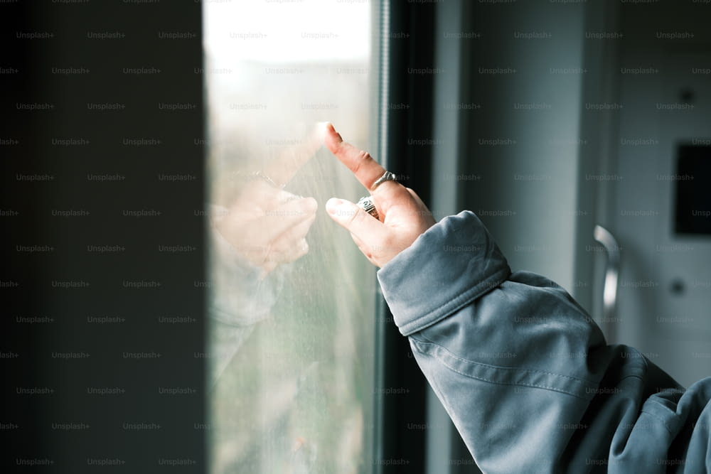 una persona in piedi davanti a una finestra con in mano un telefono cellulare