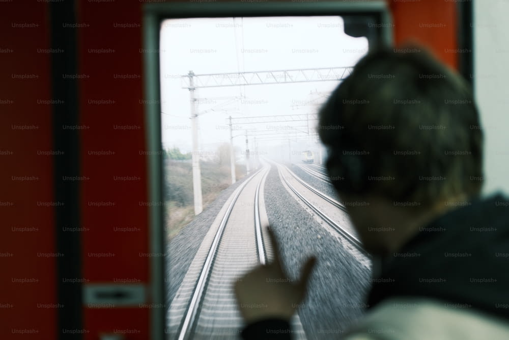 Un homme avec des écouteurs regarde par la fenêtre d’un train