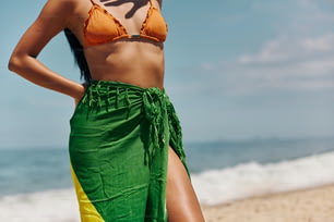 Una mujer en bikini y falda verde parada en la playa