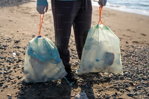 a person holding two bags of garbage on a beach