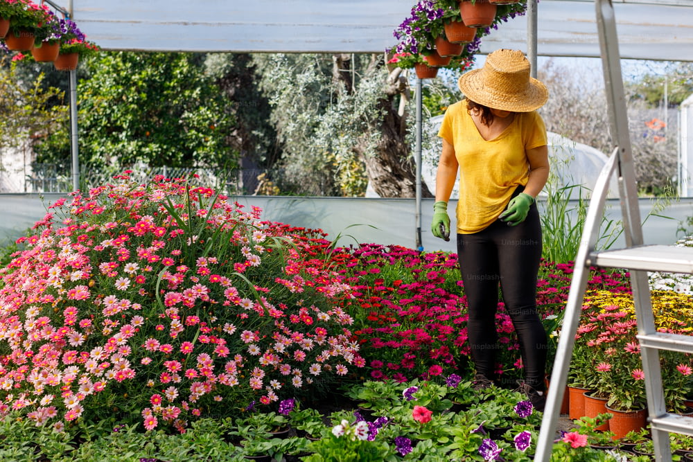 a woman in a yellow shirt and straw hat working in a garden