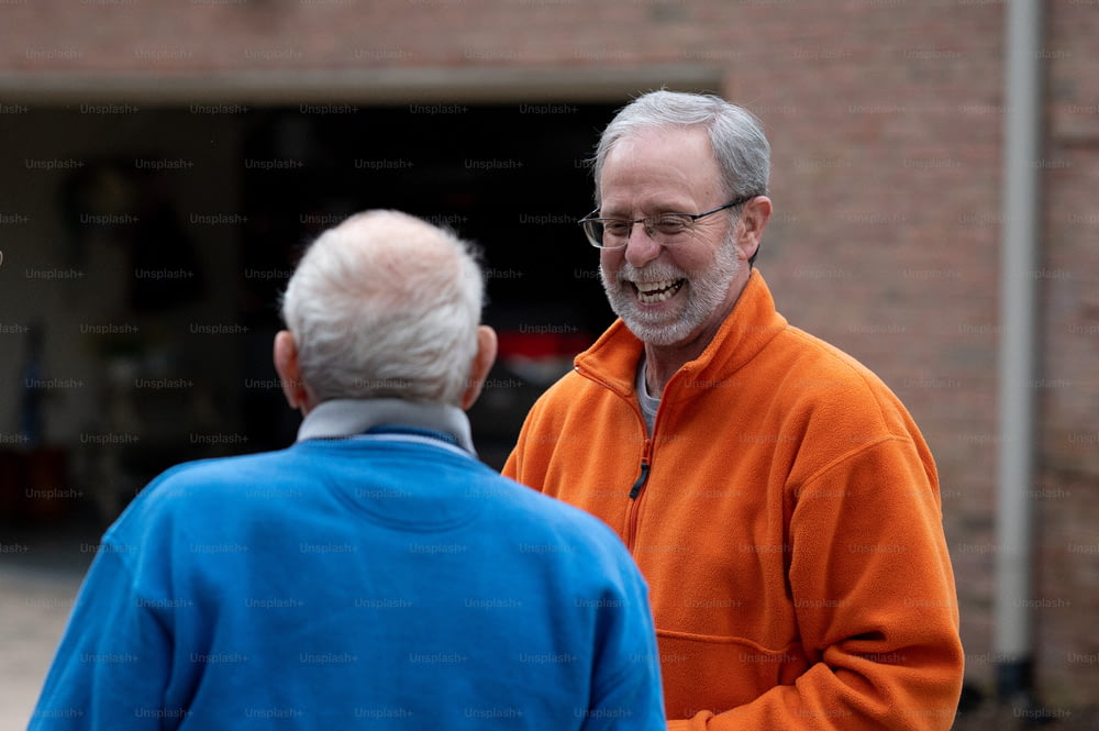 a man in an orange jacket talking to a man in a blue jacket