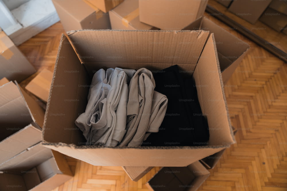 a cardboard box filled with clothes on top of a wooden floor