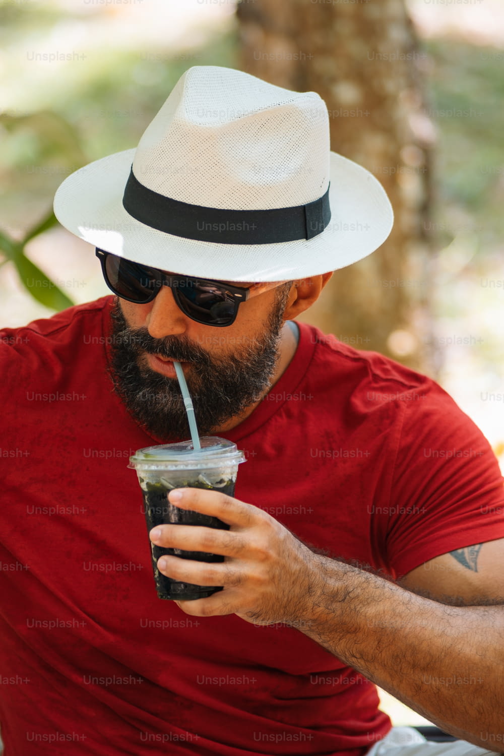 um homem com um chapéu e óculos de sol bebendo uma bebida