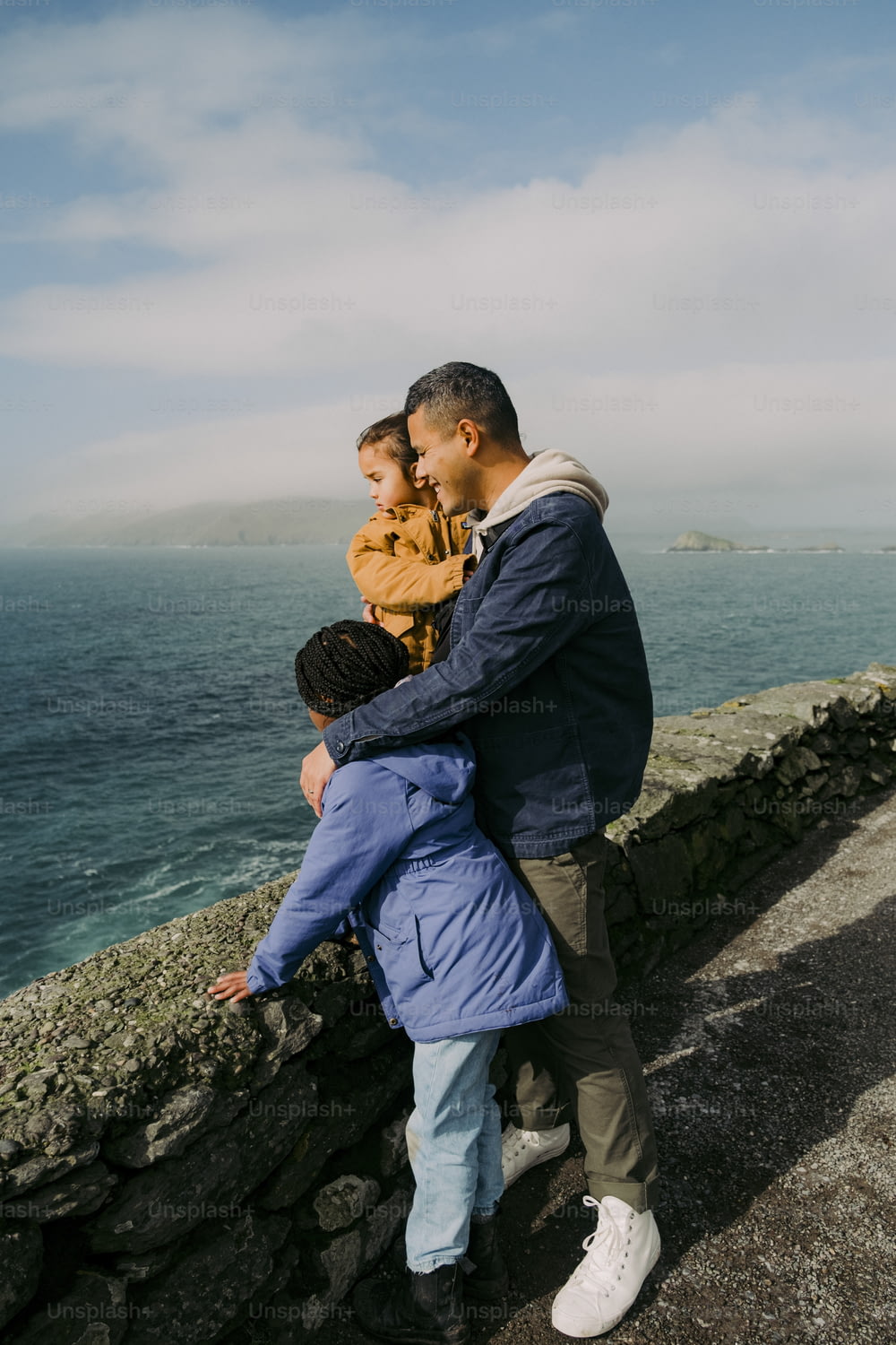 Un hombre y dos niños parados en un muro de piedra junto al océano