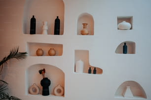 eine weiße Wand gefüllt mit Regalen gefüllt mit Vasen