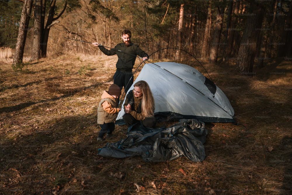 a man and woman standing next to a tent in the woods