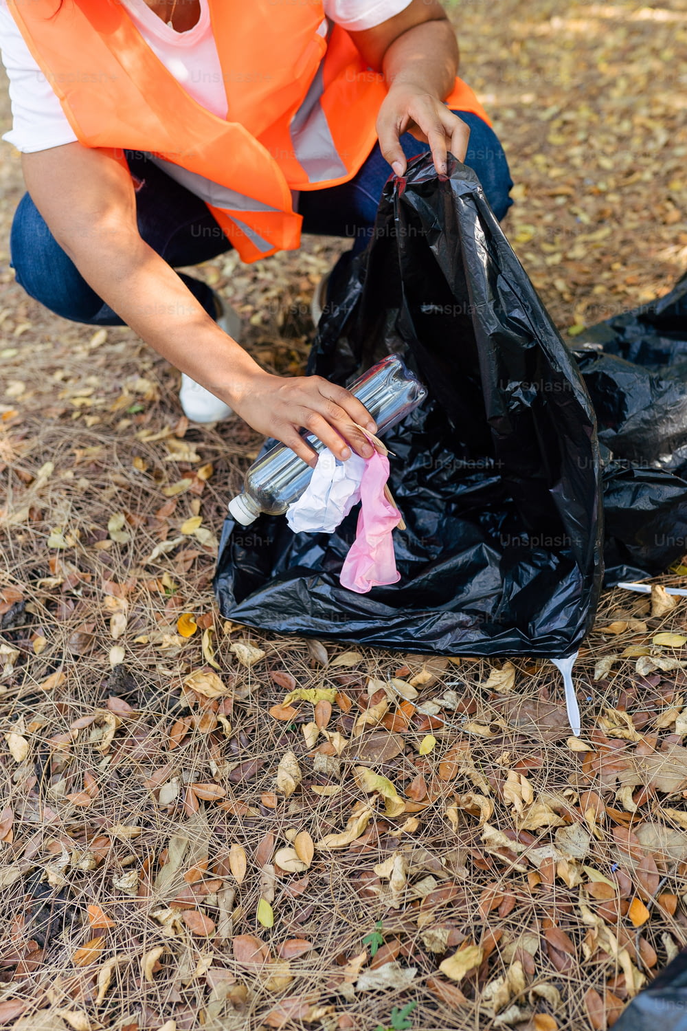 a woman in an orange vest is picking up trash
