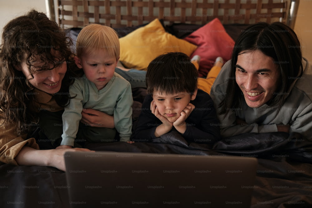 a family laying in bed looking at a laptop