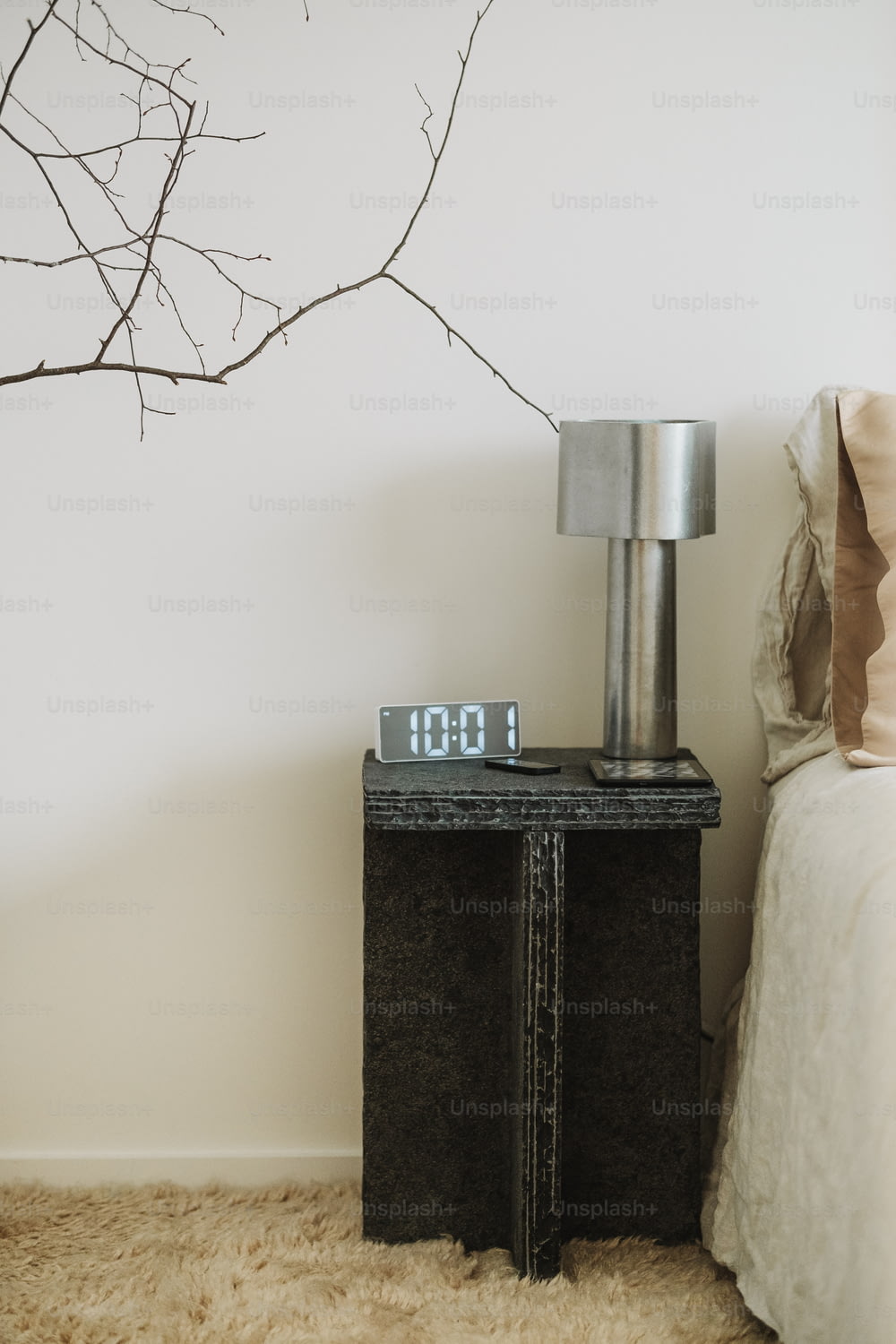 um relógio sentado em cima de uma mesa de cabeceira ao lado de uma cama