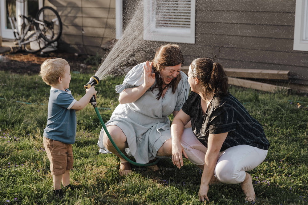 a woman and two children are playing with a hose