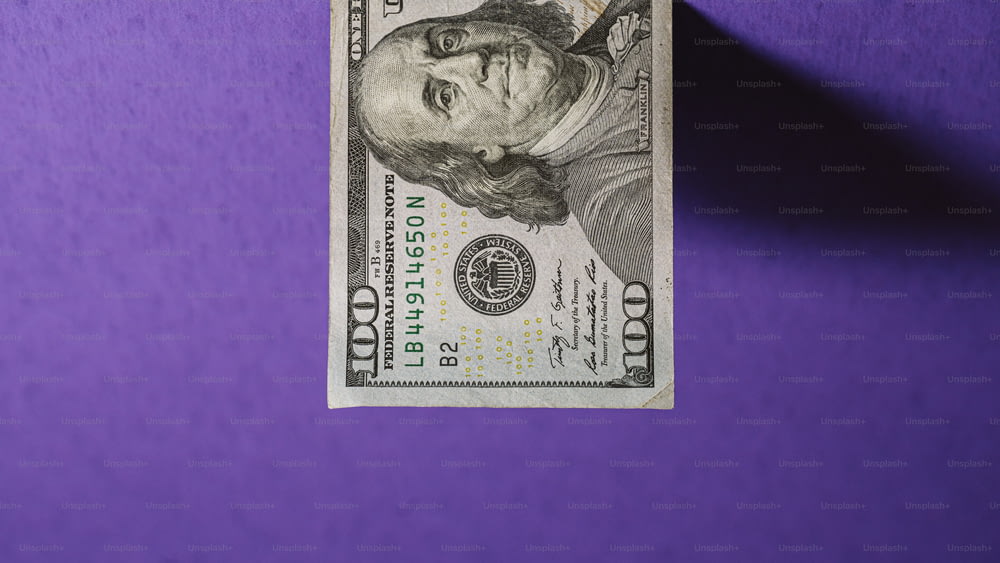 보라색 표면에 놓여 있는 100달러짜리 지폐