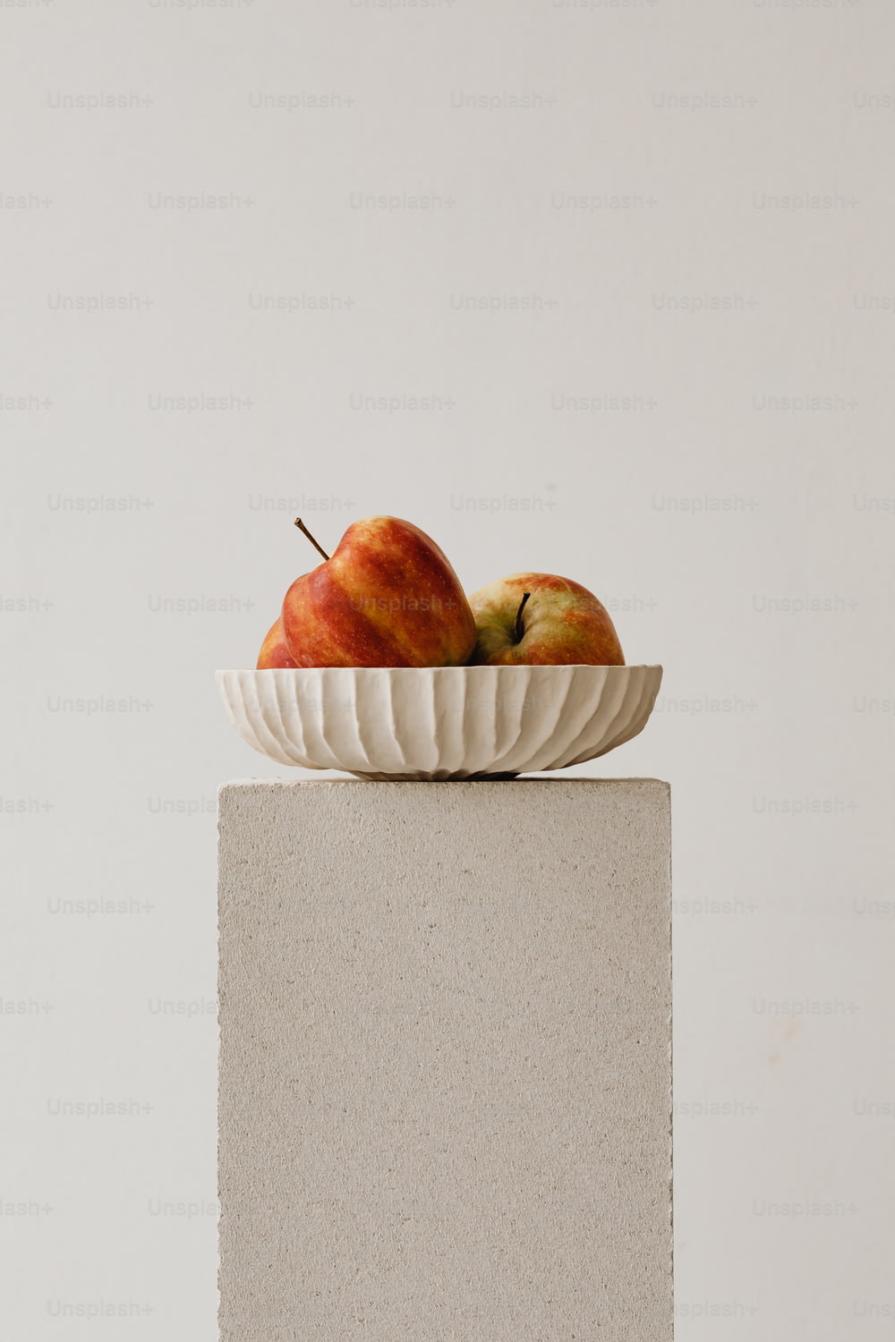 two apples in a white bowl on a pedestal