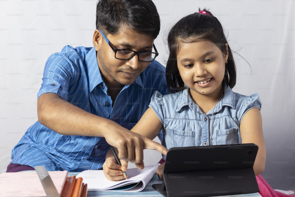 An Indian girl student studying with tablet besides her father, teacher: private teacher concept