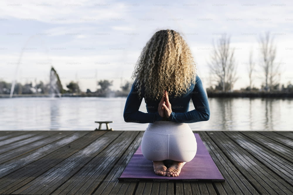 pretty blonde woman with curly hair, doing yoga relaxed on her back, on a boat dock