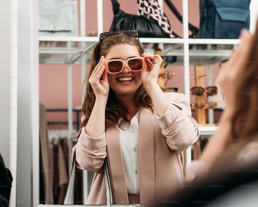 Laughing woman try on sunglasses in front of a mirror in a fashion store