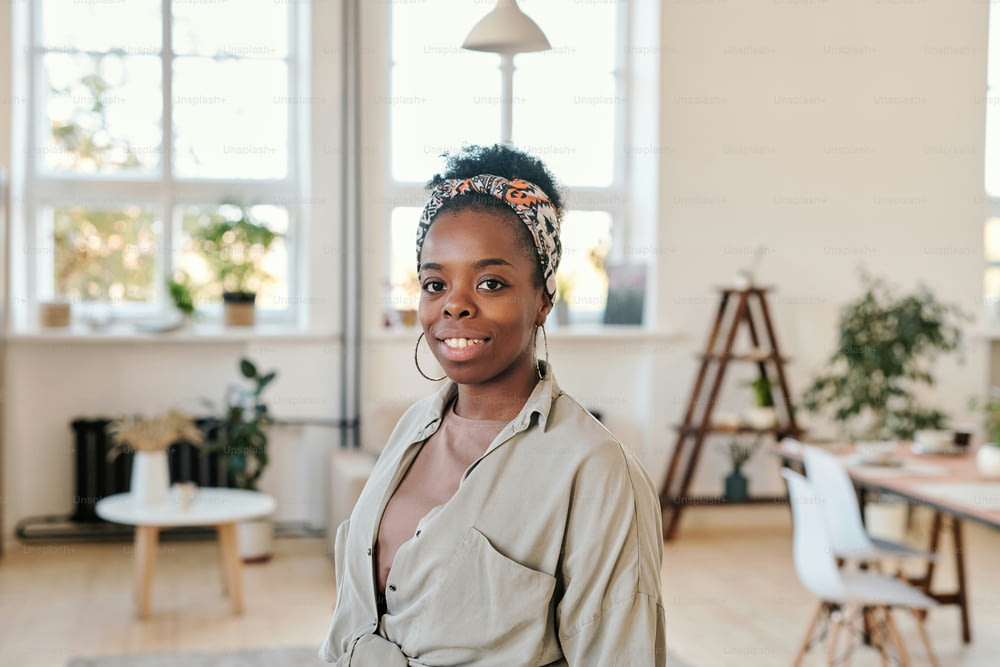 Portrait of smiling young African-American woman in headscarf and round earrings standing in modern coworking space