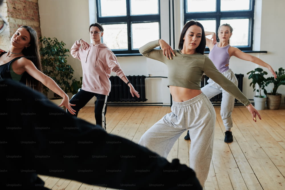 Adolescentes e cara em activewear repetindo o exercício de dança após o seu instrutor ou líder durante o treinamento no espaçoso estúdio loft