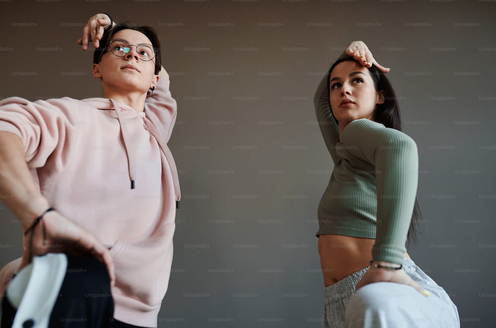 Dos adolescentes activos manteniendo sus brazos sobre la cabeza mientras entrenan nuevos movimientos de baile de moda en un estudio moderno o salón de baile