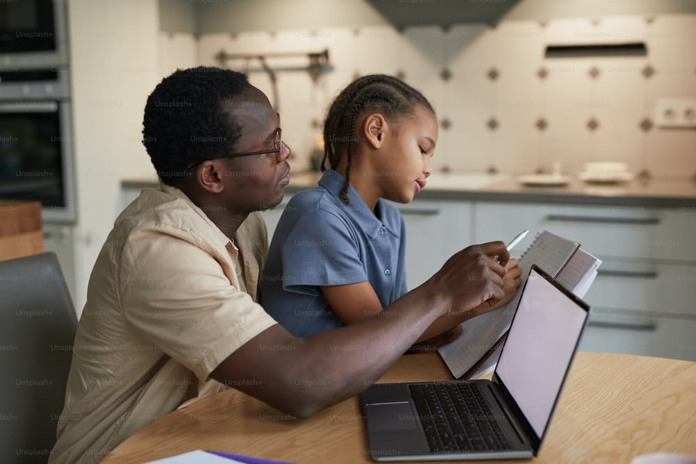 Side view portrait of caring black father helping daughter with homework in cozy scene, copy space