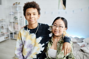 Porträt zweier Teenager der Generation Z, Junge und Mädchen, die in die Kamera lächeln und zusammen im Wohnraum posieren