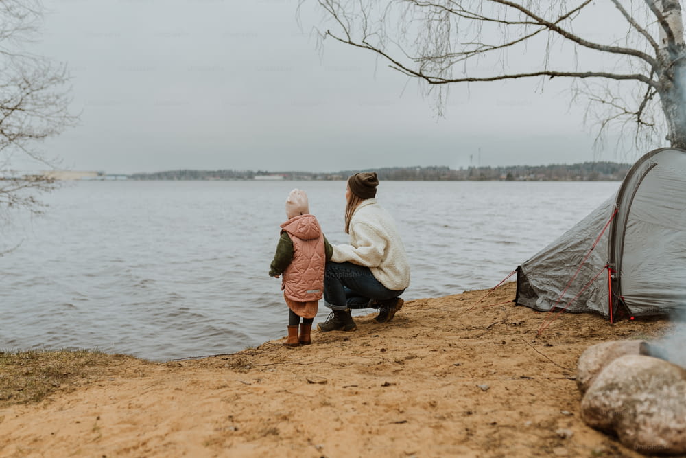 a woman and a child sitting on a beach next to a tent