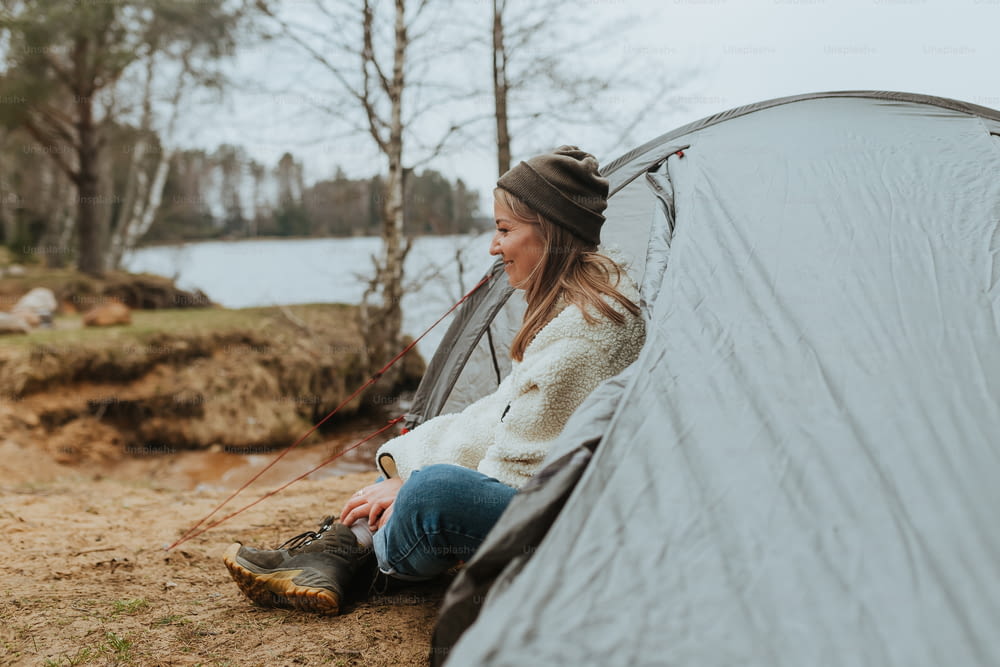 a woman sitting inside of a tent next to a lake
