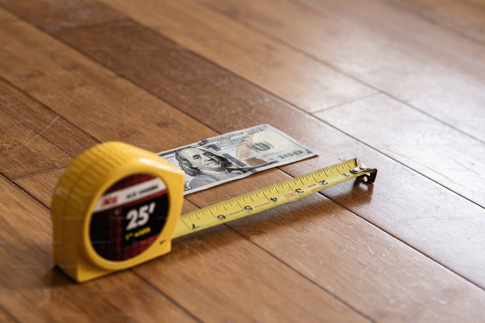 un metro a nastro e denaro su un pavimento di legno
