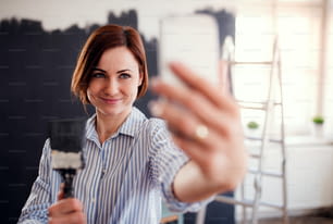 Un portrait de jeune femme créative avec smartphone peignant le mur en noir, prenant selfie. Une start-up de petite entreprise.