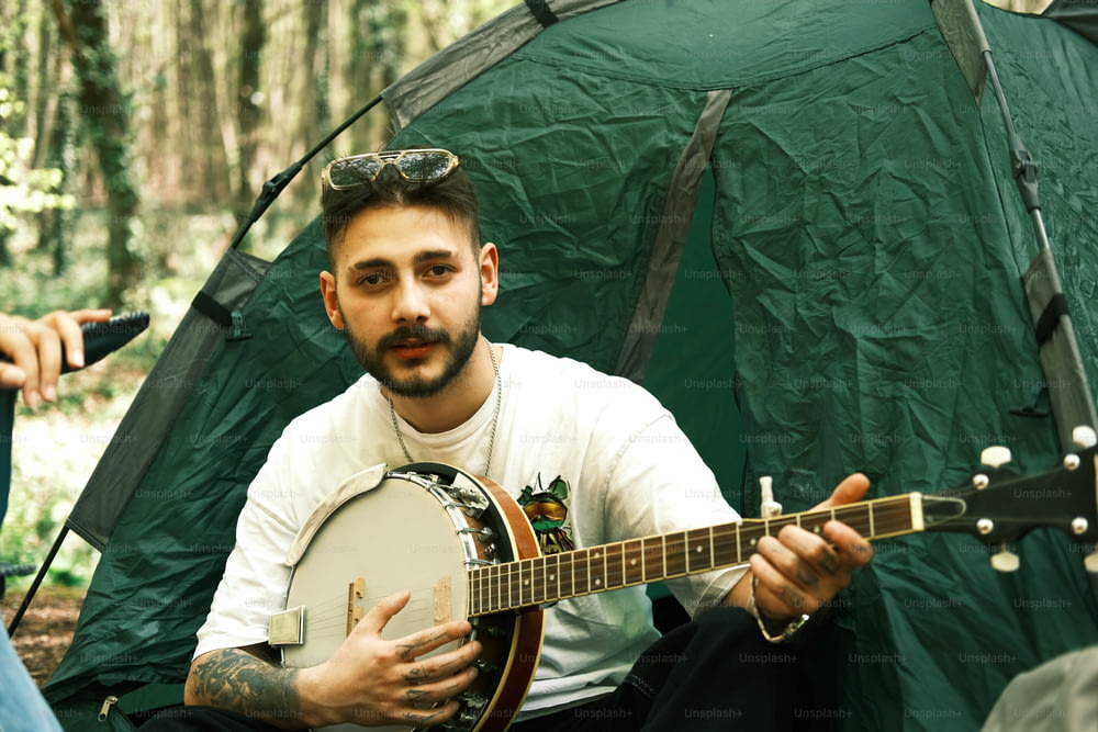 a man sitting in front of a tent holding a guitar