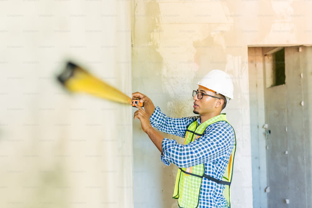 a man in a hard hat and safety vest spraying cement on a wall