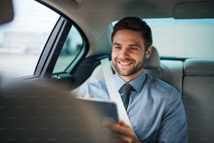 タブレットを持つビジネスマンが車の後部座席に座って働いている。