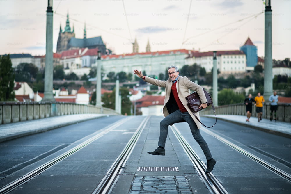 Ein glücklicher, reifer, gutaussehender Geschäftsmann mit Tasche, der eine Straße in Prag überquert.