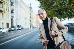 Uomo d'affari maturo con borsa in piedi sulla strada nella città di Praga, in attesa di un taxi. Copia spazio.