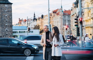 Mature man and young woman business partners crossing a busy road in city of Prague, talking.