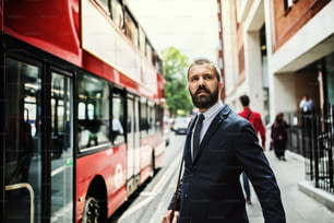 Hombre de negocios hipster serio parado en la calle, esperando el autobús en Londres.